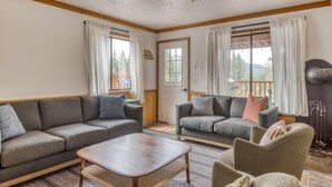 Un salon comprenant deux canapés, une table basse et un fauteuil, avec un plafond en bois et une vue sur l’extérieur.