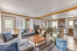 A living room with a sofa, armchairs, a coffee table, and a kitchen area with a stove, sink, and cabinets.