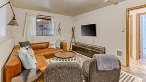 Un salon comprenant un canapé, des fauteuils, une table basse, un téléviseur à écran plat et une fenêtre avec des rideaux.