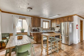 A kitchen with wooden cabinets, a stainless steel refrigerator, and a dining area with a wooden table and green chairs.