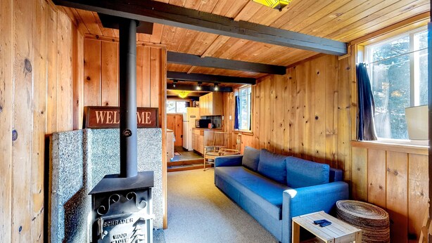 A wooden cabin interior with a wood stove, a sofa, a dining area, and a kitchen. - Cozy, comfortable cottage in Government Camp (Government Camp)
