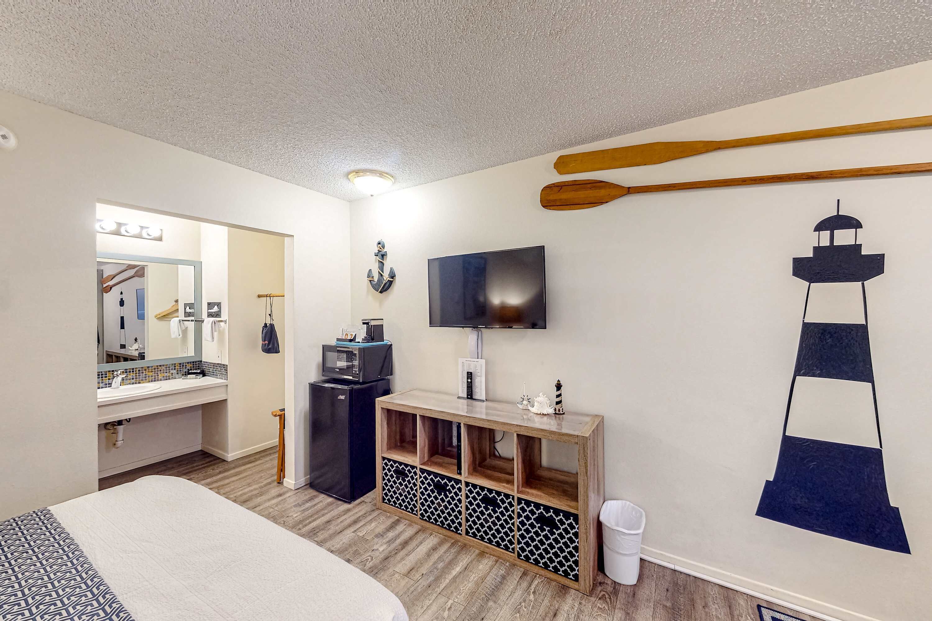 A hotel room with a bed, a TV, a wooden console, a mirror, and a wall decoration.