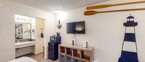 A hotel room with a bed, a TV, a wooden console, a mirror, and a wall decoration.
