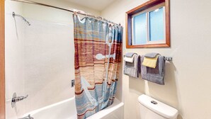 Une salle de bain avec un rideau de douche, des toilettes, une fenêtre et des serviettes rangées sur un porte-serviettes.