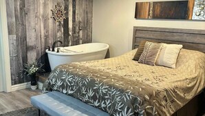 A bedroom with a wooden wall, a bathtub, a bed with patterned bedding, and a bench.