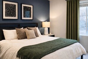 Un lit bien fait, avec des oreillers, une lampe de chevet et deux œuvres d’art encadrées accrochées au mur.