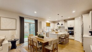 A modern kitchen with white cabinets, a dining area with a wooden table and chairs, and a view of the outdoors through a large window. - Spacious family friendly home with full kitchen, enclosed yard, washer & dryer (Eugene)