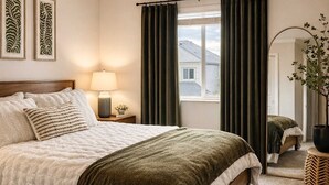 A bedroom with a bed, a nightstand with a lamp, a window with curtains, and a mirror. - Spacious family friendly home with full kitchen, enclosed yard, washer & dryer (Eugene)