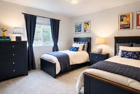 A bedroom with two beds, a dresser, a nightstand, a window with curtains, and wall art. - Spacious family friendly home with full kitchen, enclosed yard, washer & dryer (Eugene)