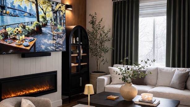 A modern living room with a fireplace, a sofa, a coffee table, and a television displaying a scenic outdoor view. - Spacious family friendly home with full kitchen, enclosed yard, washer & dryer (Eugene)
