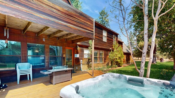 Terraza de madera con hidromasaje, mobiliario exterior y vista a una casa moderna.