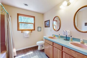 Ein Badezimmer mit einem Holzkosmetikschrank, einem Waschbecken, einer Toilette, einem Fenster und einem Spiegel.
