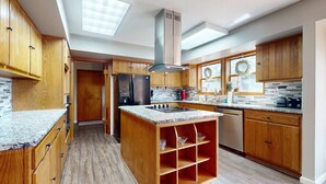 Una cocina moderna con gabinetes de madera, encimera de granito, horno empotrado y campana extractora de acero inoxidable.