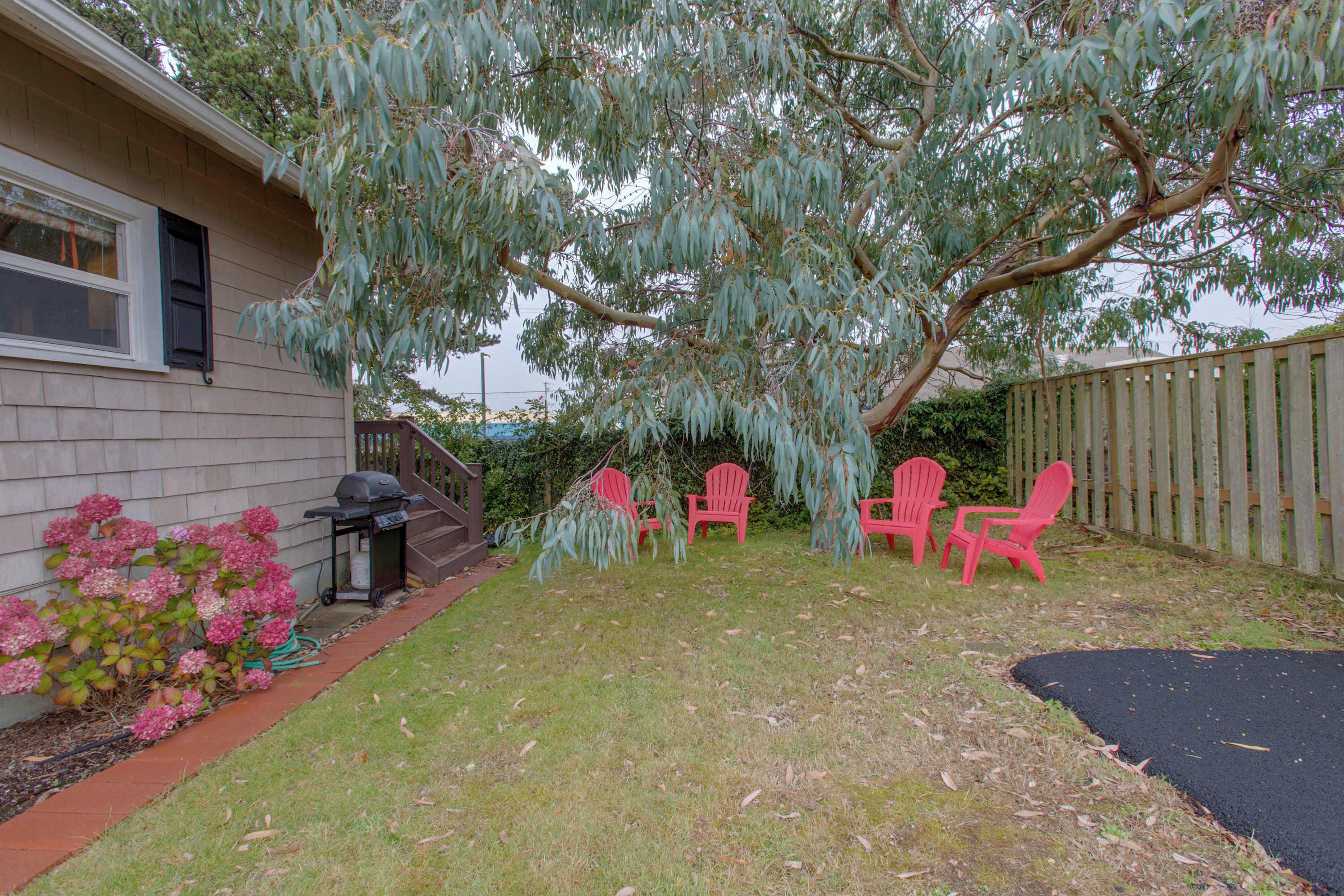 A backyard with a tree, a barbecue grill, and red chairs.