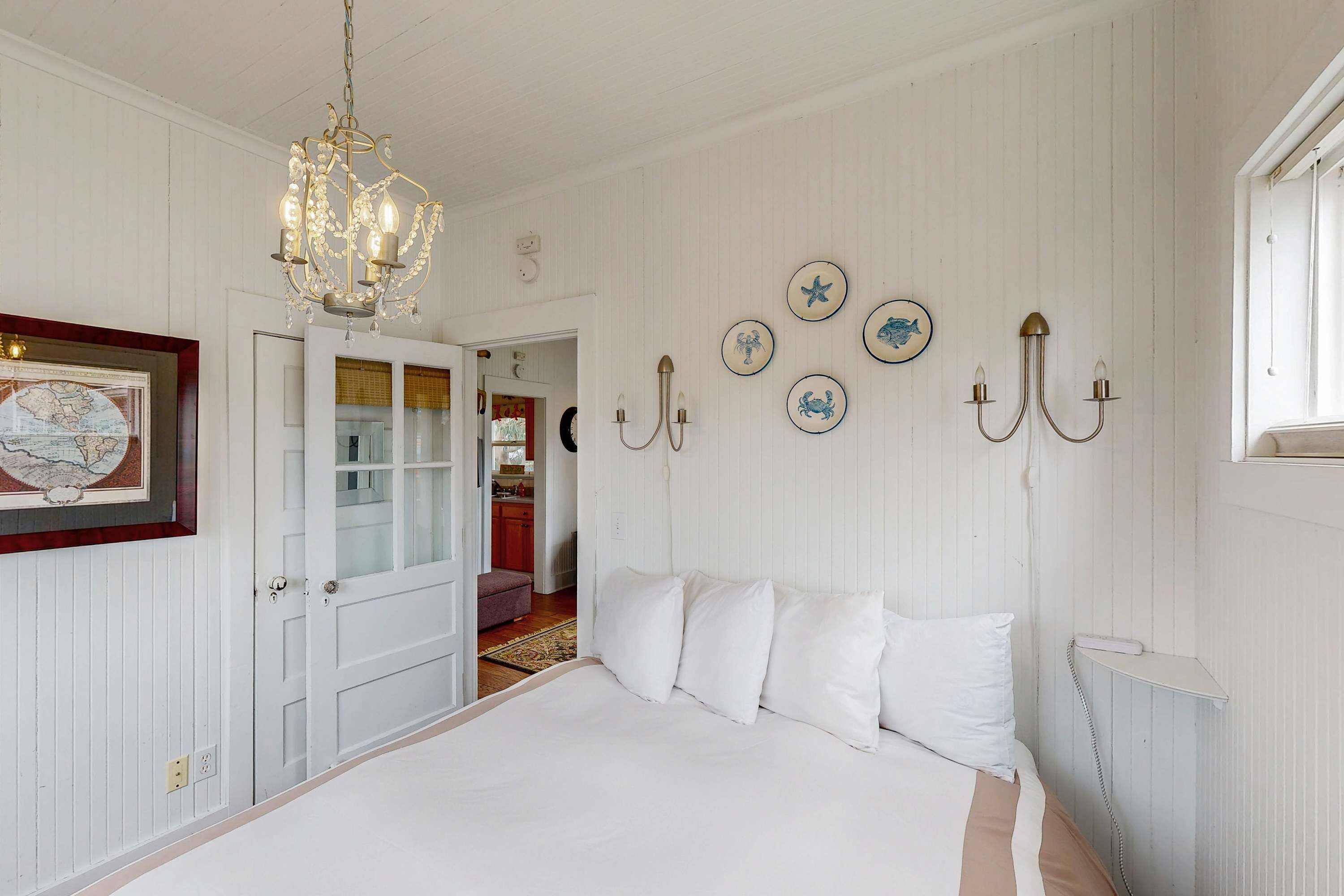 Une chambre à coucher avec un grand lit, un lustre, des appliques murales et une porte donnant sur une autre pièce.