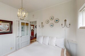 A bedroom with a large bed, a chandelier, wall-mounted lights, and a door leading to another room. - Dog-friendly cottage with great location, cozy interior, WiFi & washer/dryer (Seaside)