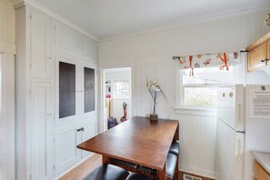 A kitchen with white paneled walls, a wooden table, and a window with a curtain. - Dog-friendly cottage with great location, cozy interior, WiFi & washer/dryer (Seaside)
