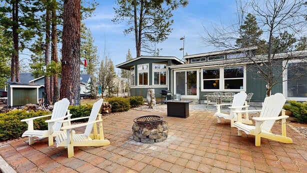 Een terras met Adirondack-stoelen, een vuurkorf van steen en een gebouw met grote ramen.