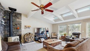 Een woonkamer met een stenen open haard, een plafondventilator, een televisie en een groot raam.