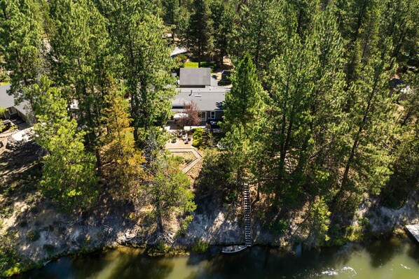 An aerial view of a house surrounded by dense forest, with a dock extending into a body of water. - Pet friendly home steps to Deschutes River with hot tub, foosball & play set (Bend)