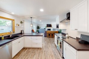 A modern kitchen with white cabinetry, a central island, a built-in oven, and a dining area with a wooden table.