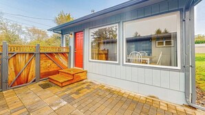 Uma casa com porta vermelha, um portão de madeira e um pátio pavimentado.