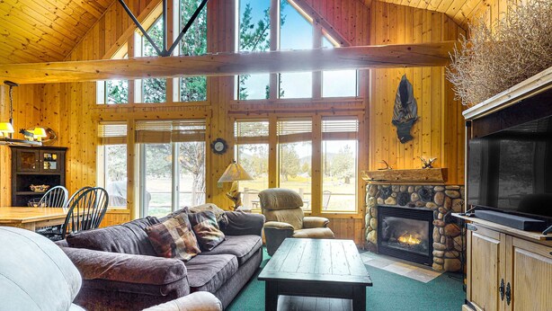Interior acogedor de una cabaña con chimenea de piedra, muebles de madera y ventanas amplias.