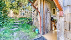 Un bâtiment rustique en bois, doté d’une porte en bois, d’un petit porche et d’un intérieur visible avec des étagères et une machine à café.
