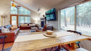 A spacious living room with a large wooden table, leather sofas, and a fireplace. - Gorgeous home with private hot tub, SHARC passes, bikes, WiFi, streaming (Sunriver)