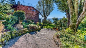 Un camí de pedra que condueix a una casa envoltada de vegetació i arbres frondosos.