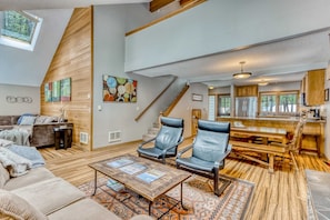 A spacious living area with a wooden floor, leather chairs, a coffee table, and a kitchen in the background. - All-season resort home with on-site pool, hot tub, gym, golf, & fireplaces (Black Butte Ranch)