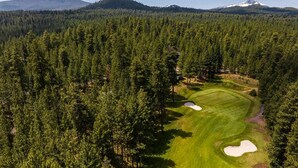 Golfkenttä, jonka ympärillä on tiheää metsää ja taustalla kohoaa vuori.