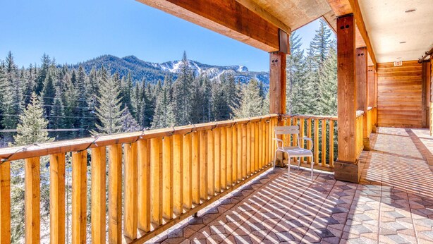 Un balcón de madera con vistas a montañas nevadas y pinos.