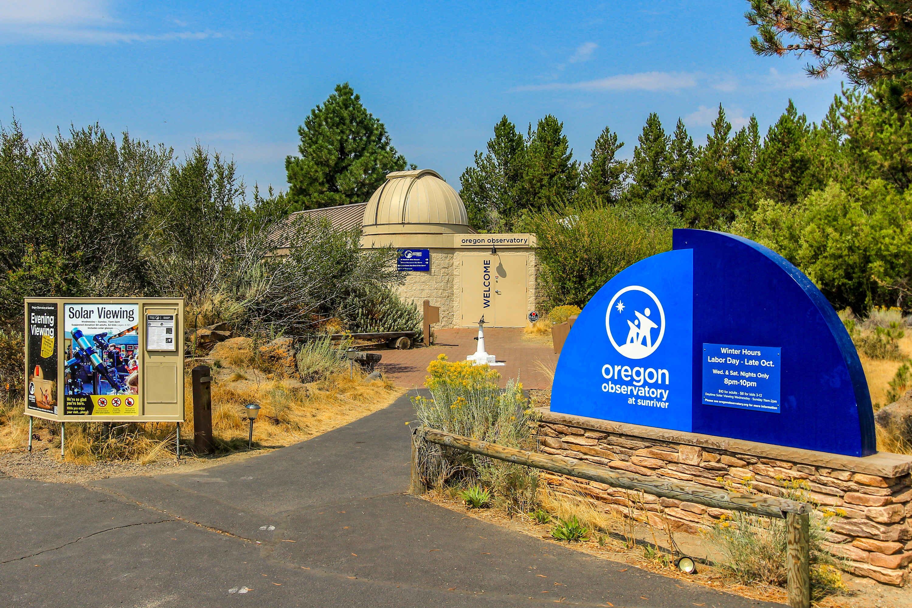 An entrance to the Oregon Observatory at Sunriver with a signboard and a blue archway.