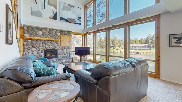Ein geräumiges Wohnzimmer mit Kamin aus Stein, Ledersofas, einem runden Couchtisch und großen Fenstern mit Blick ins Freie.