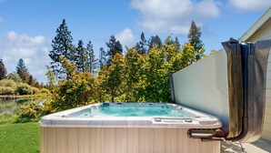 Ein Whirlpool mit Holzverkleidung, draußen gelegen mit Blick auf Bäume und ein Gewässer im Hintergrund.