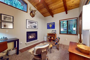 A cozy living room with a fireplace, wooden ceiling, and a deer head decoration.