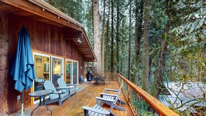 Eine Holzterrasse mit Adirondack-Stühlen, einem Tisch und einem blauen Sonnenschirm.