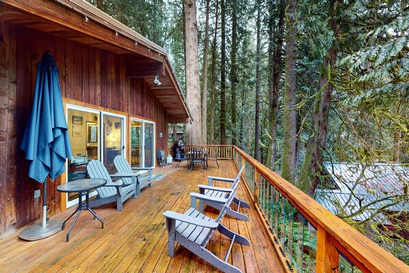 A wooden deck with Adirondack chairs, a table, and a blue umbrella.