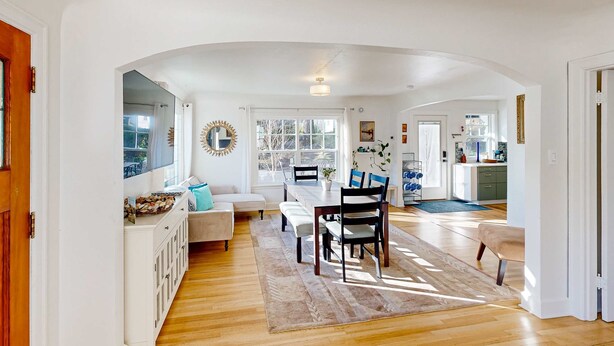 An open-plan living and dining area with a wooden floor, white walls, a dining table with chairs, a sofa, and a bench. - Renovated home in central location with hot tub, theater, fast wifi & work desks (Stevenson)