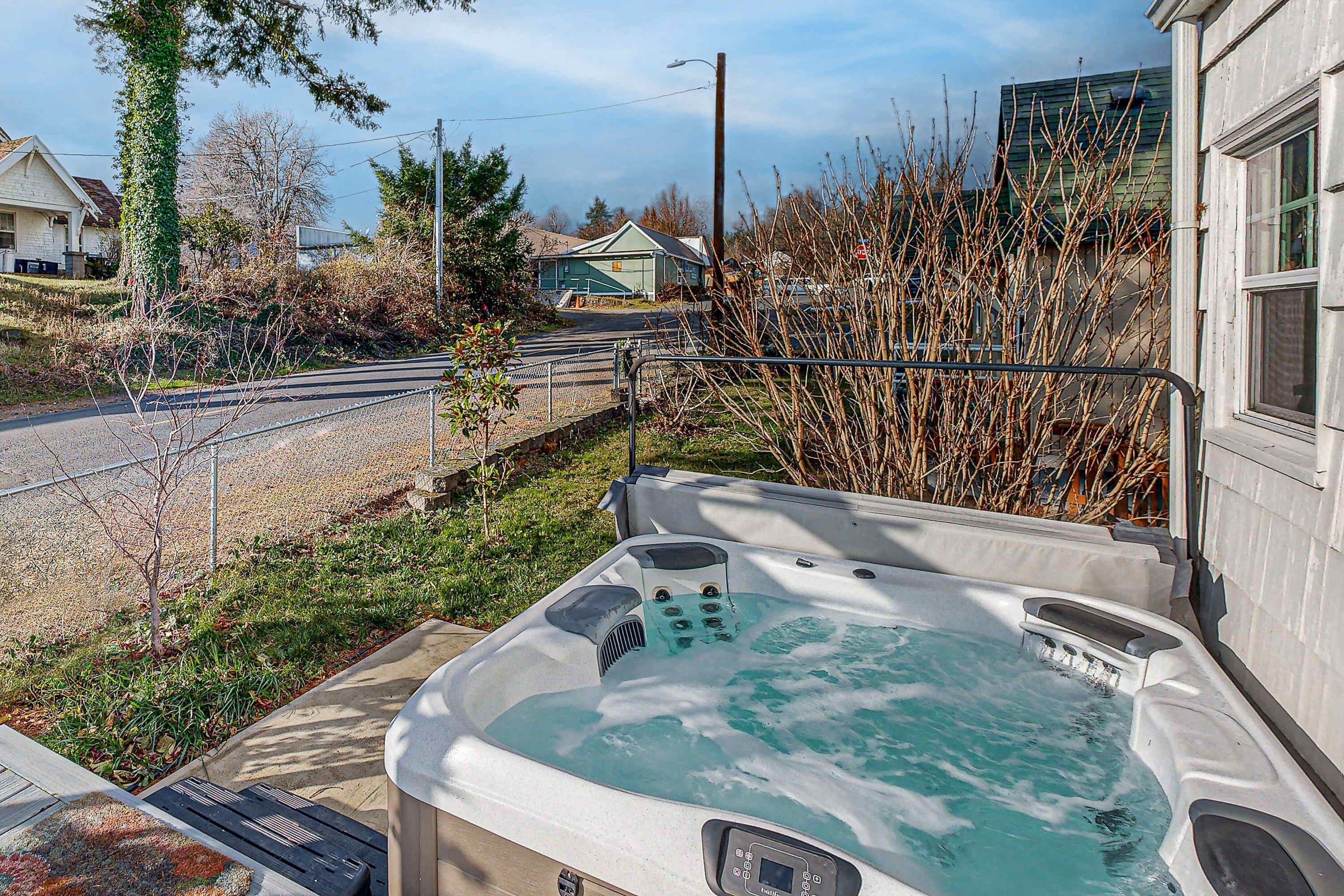 Un bain à remous doté d’un panneau de commande, d’une terrasse en bois et offrant une vue sur une route et des maisons.
