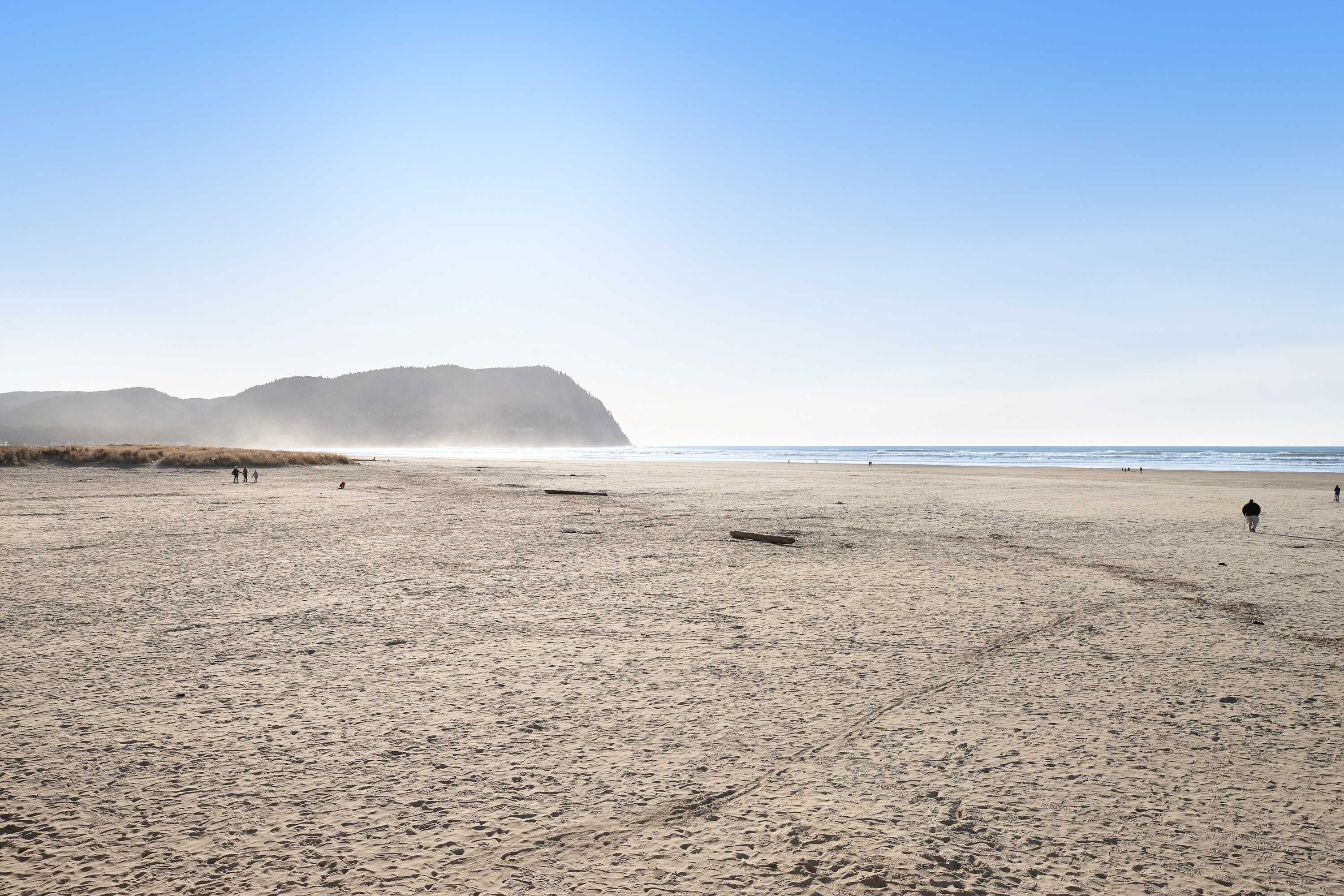 A wide sandy beach with footprints and a distant mountain.