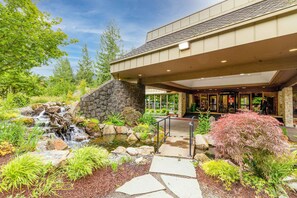 A hotel entrance with a stone waterfall, a stone pathway, and a large window overlooking the garden. - Expansive golf-view getaway with private hot tub, pool, fast WiFi & game room (Welches)