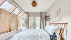 Une chambre à coucher avec un lit, une chaise, une décoration murale en macramé et de grandes fenêtres.