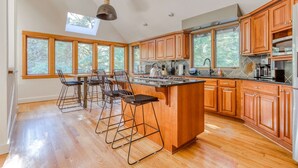 Une cuisine moderne avec des meubles en bois, un îlot central, des tabourets de bar et de grandes fenêtres.
