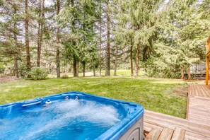 A hot tub on a wooden deck with a grassy yard and pine trees in the background. - Expansive golf-view getaway with private hot tub, pool, fast WiFi & game room (Welches)