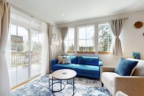 A living room with a blue sofa, a round coffee table, and a wicker chair. - Quaint second floor home one mile from the ocean; with full kitchen & W/D (Manzanita)