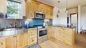 Une cuisine moderne avec des meubles en bois, des appareils électroménagers en acier inoxydable et des luminaires suspendus.