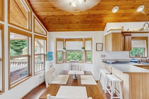 Cocina con paneles de madera, comedor, ventanas amplias y vistas al exterior.