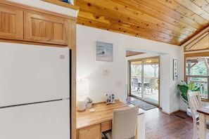 Una cocina con armarios de madera, encimera de madera, un refrigerador, una mesa con sillas, una lámpara, una planta en maceta y una ventana con vistas al exterior.